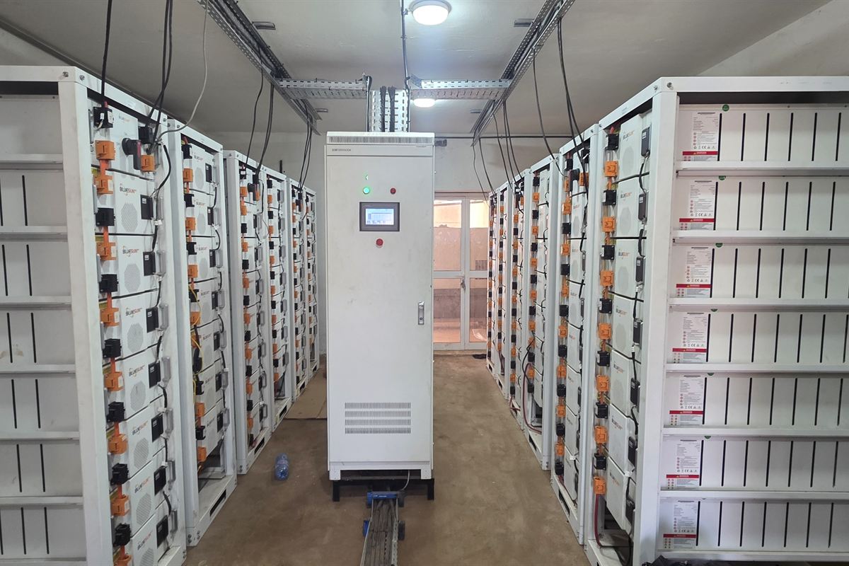 Salle de stockage : baies de batteries alignées de chaque côté d'une allée, armoire de commande au fond